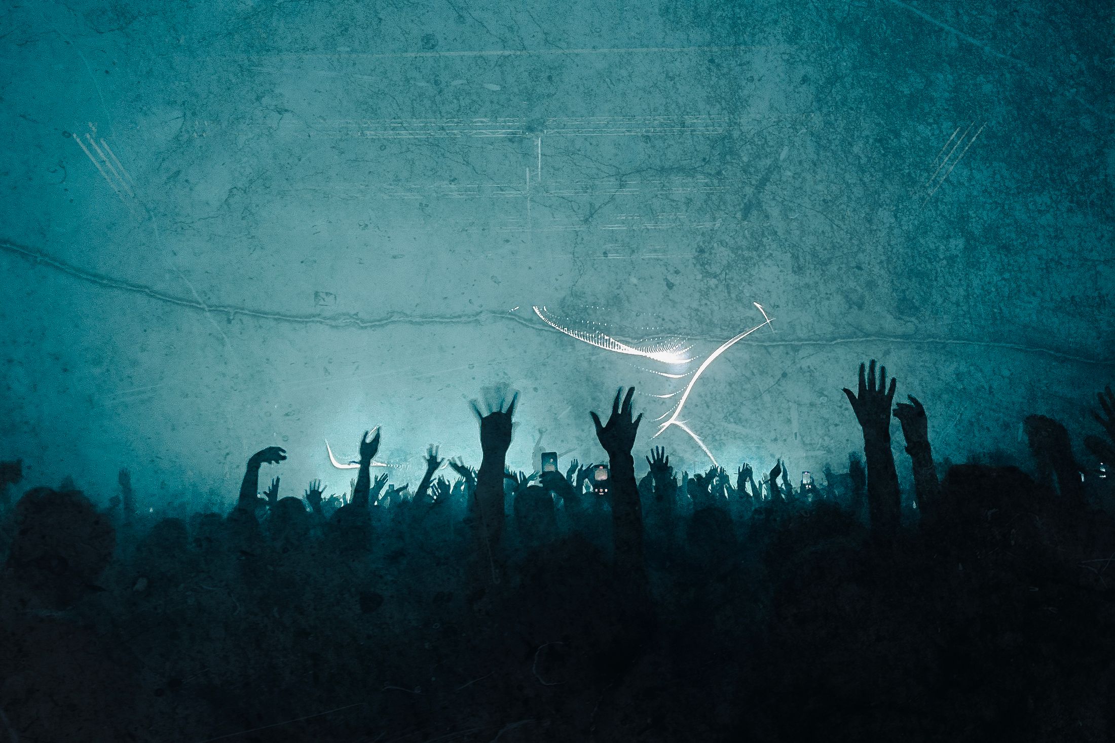 A festival crowd reaching toward the light through stage haze